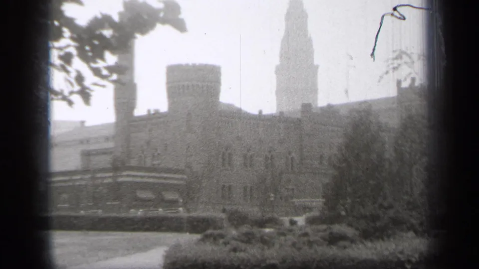 1938 Cleveland 8mm frame with a stone institutional-looking building, round turret, pointed tower, trees, and landscaped foreground.