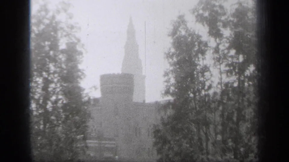 1938 Cleveland 8mm frame emphasizing the turret and tall spire of a stone building, with trees obscuring parts of the view.