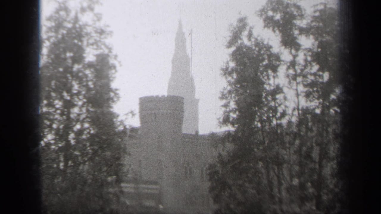 1938 Cleveland home-movie frame showing a snowy exterior view of a towered stone building partly obscured by trees and a window frame.