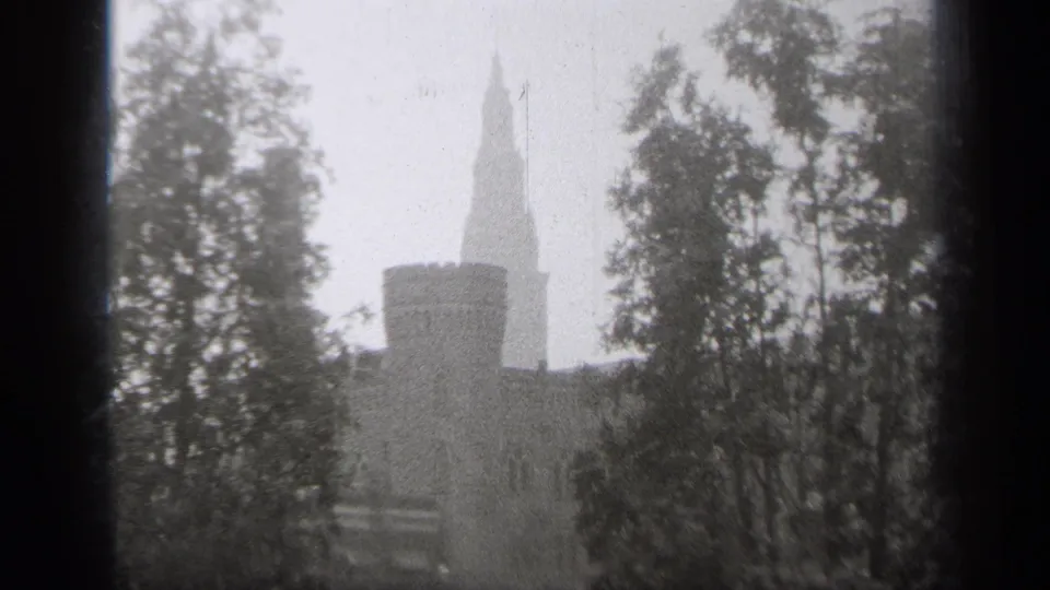 1938 Cleveland home-movie frame showing a snowy exterior view of a towered stone building partly obscured by trees and a window frame.