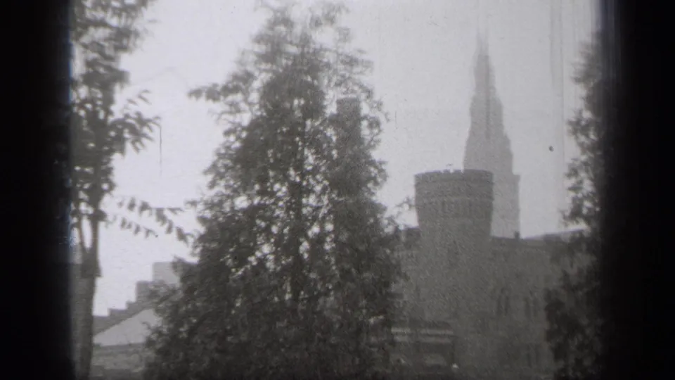 A grainy 8mm frame from Cleveland in 1938 shows trees crossing a snowy view of a stone building and tall spire.
