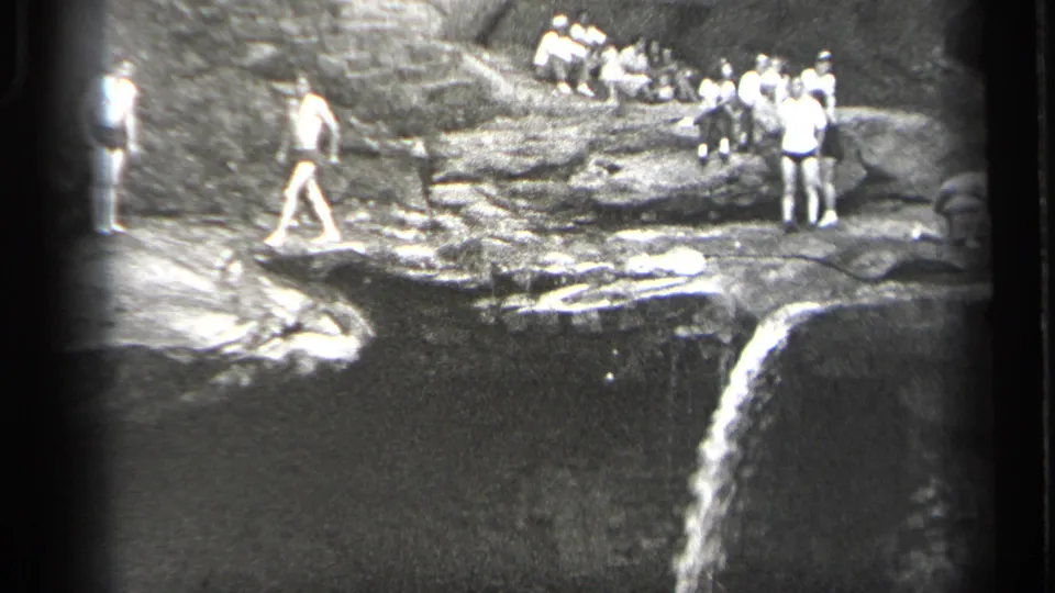 1938 Cleveland-area home-movie frame showing men gathered on rocky ledges above a waterfall and pool.