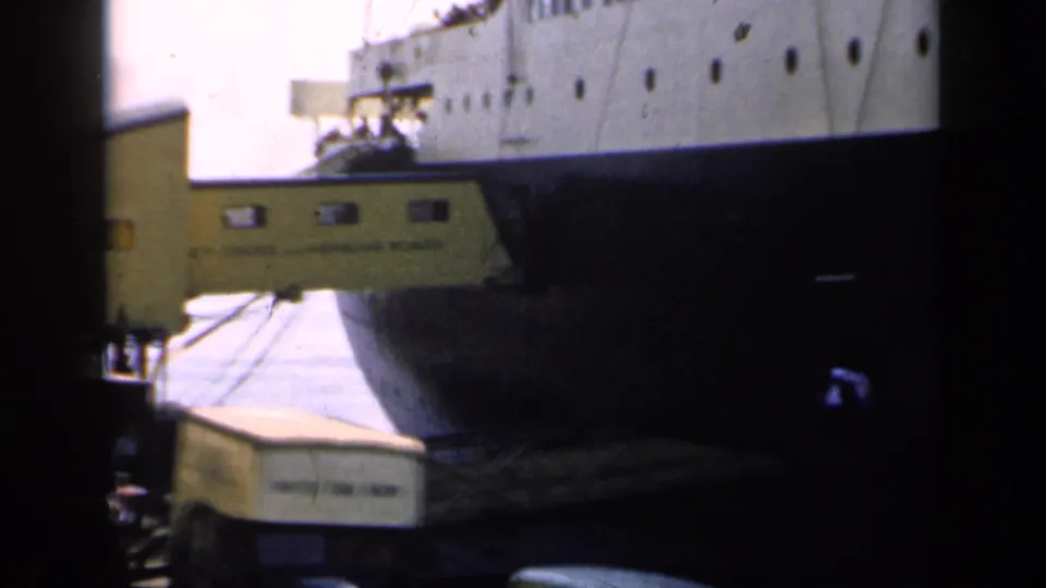 1949 England dock view showing the liner's dark bow, yellow gangway, and a light-colored luggage container near the pier.