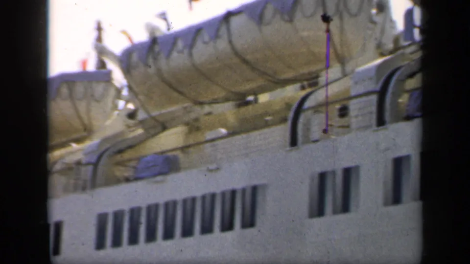 Soft 8mm frame from England in 1949 showing the ship's upper deck, covered lifeboats, railing, and dark window rows.