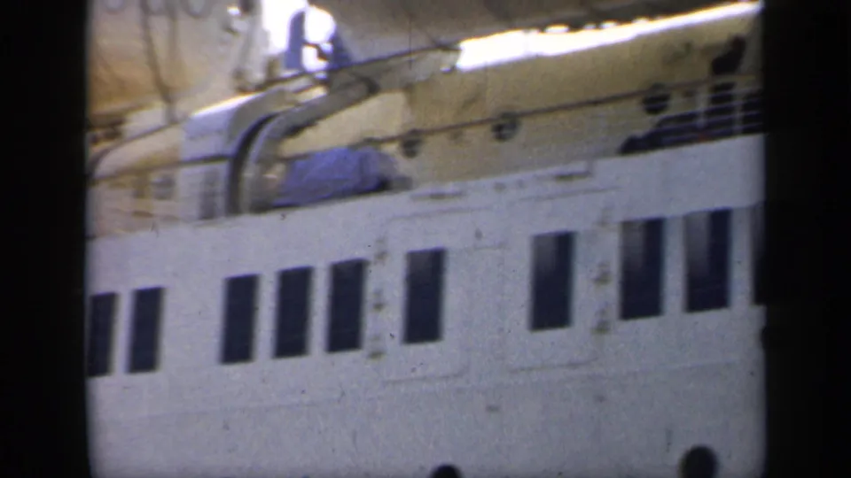 1949 England frame showing a close dockside section of a white passenger ship, with lifeboat covers, rails, vents, and dark windows.
