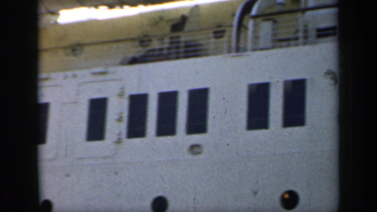 1949 England 8mm frame showing a close, slightly soft view of a white passenger ship hull with dark windows and circular portholes.