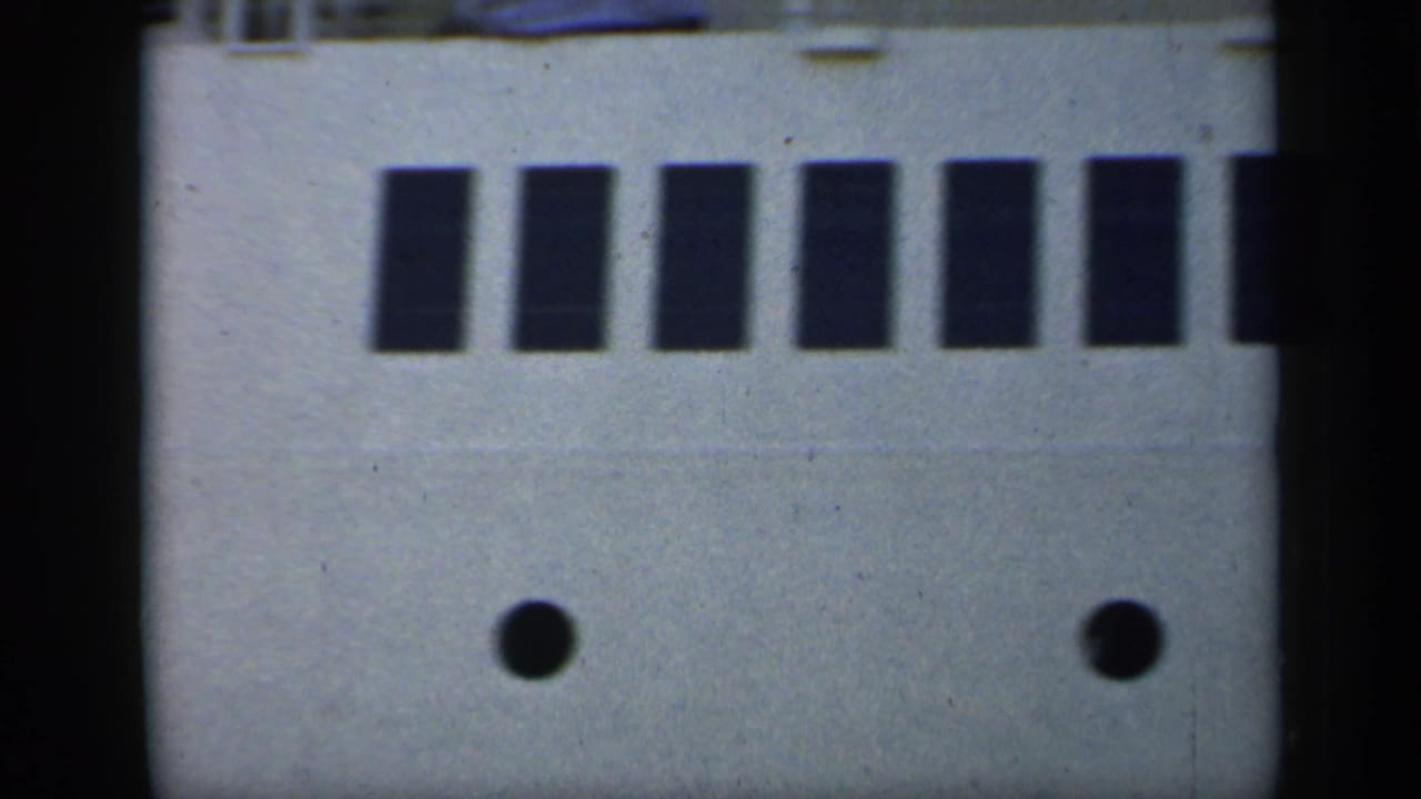 1949 England 8mm frame showing the side of a large passenger ship with dark windows, round portholes, and a cropped upper deck.
