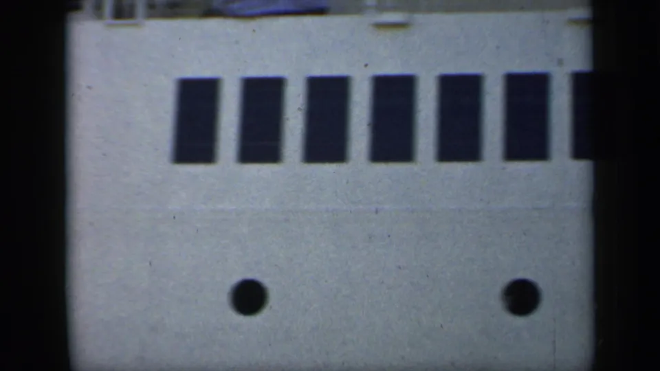 1949 England 8mm frame showing the side of a large passenger ship with dark windows, round portholes, and a cropped upper deck.