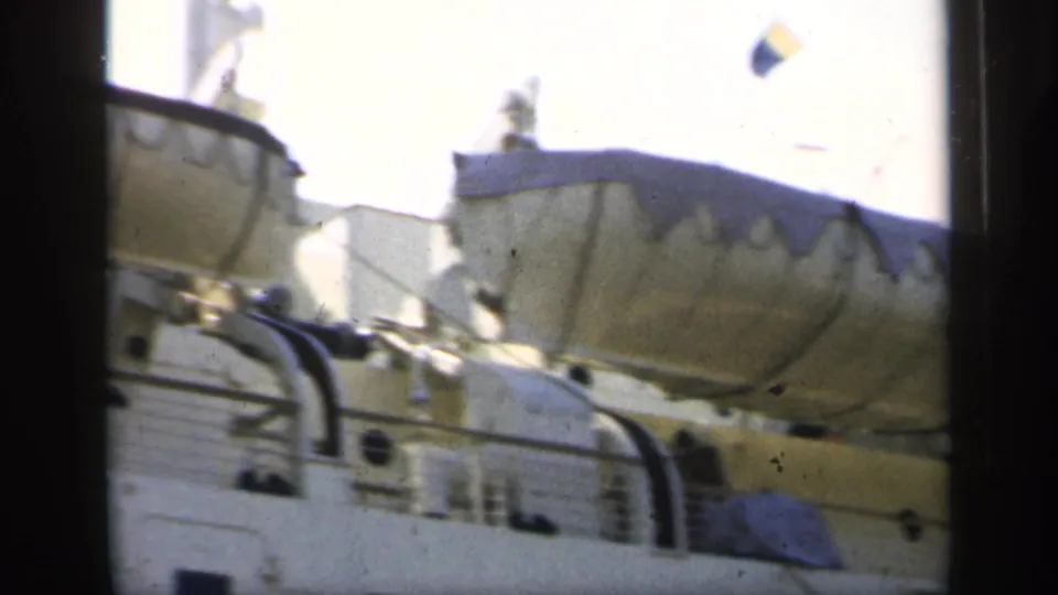 1949 England 8mm frame showing covered lifeboats, deck railings, and upper structures on a large passenger ship under bright light.