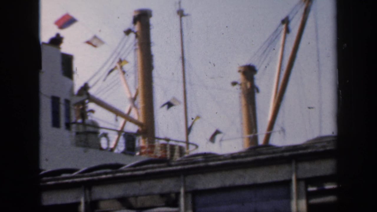 Cargo ship rigging and flags seen through a dark foreground frame.