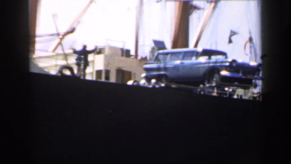 1949 England home-movie frame with a deck worker near a blue station wagon on a cargo ship.