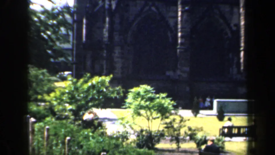 The final frame shifts to a nearby exterior area with greenery, benches, stone or structural details, and small people in the distance.