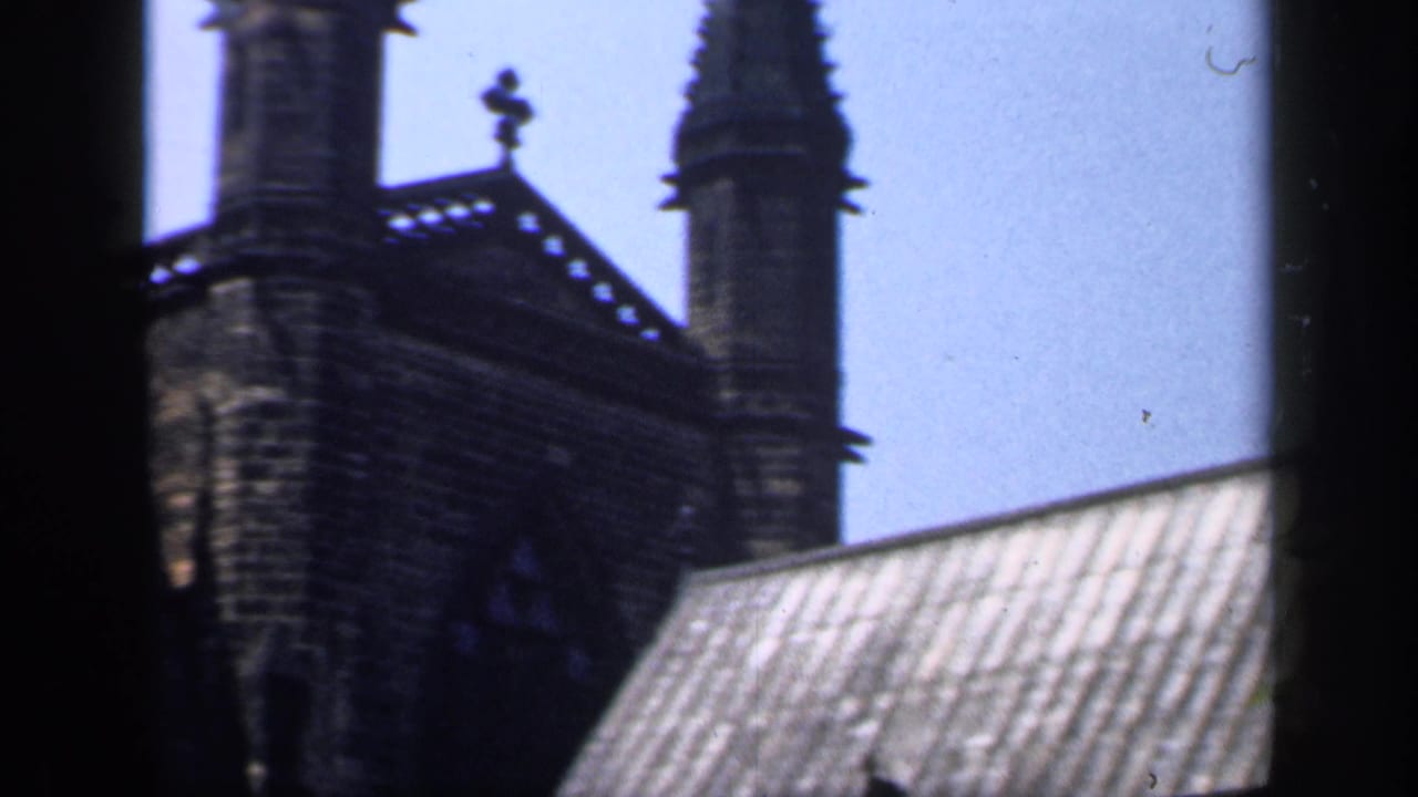 Dark-framed view of church spires and stonework above a pale roof.