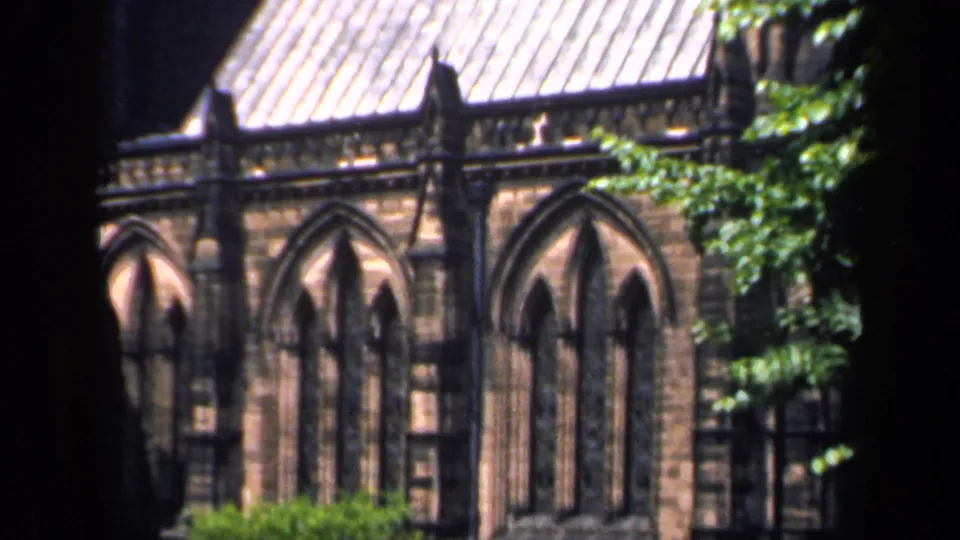 1949 England 8mm frame showing pointed arched church windows, weathered masonry, roofline, and foliage.