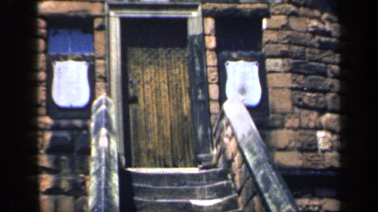 Closer view of the wooden door, stone steps, railing, and flanking windows.
