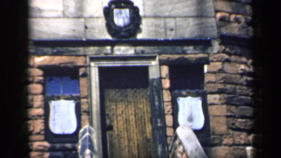 1949 England frame showing the upper part of the entrance, including masonry, covered windows, and a dark crest above the door.