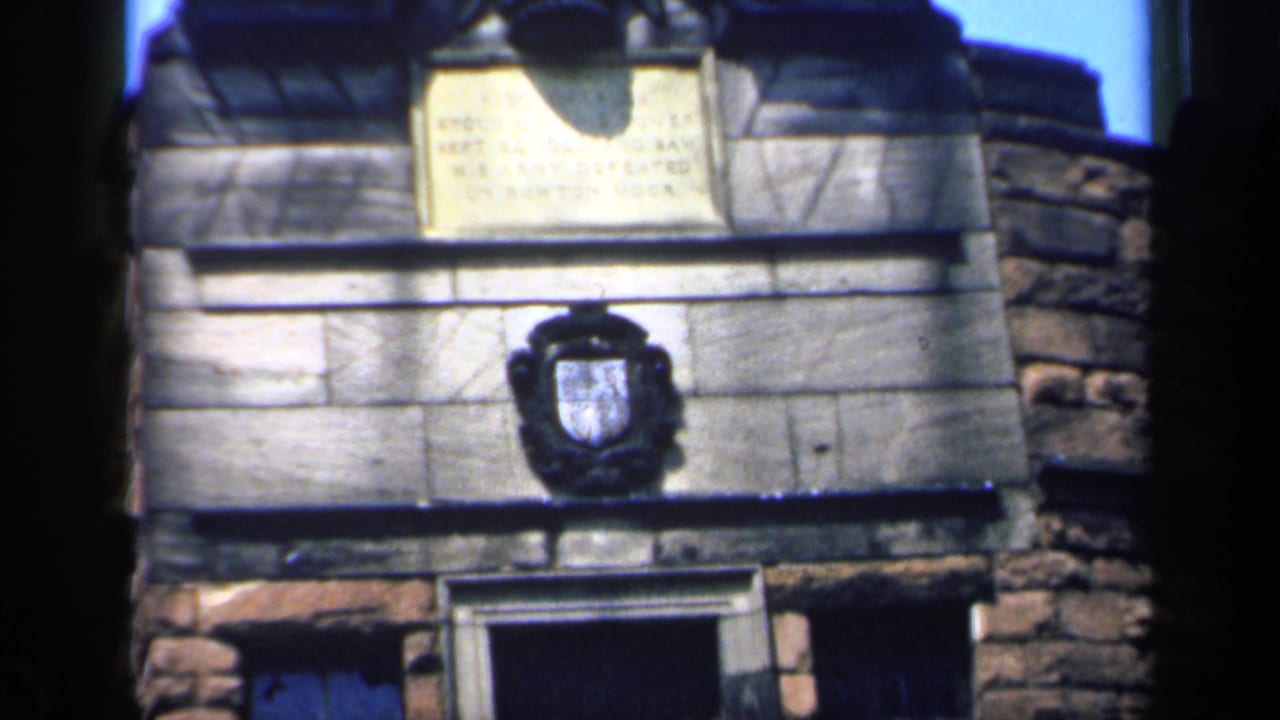Stone facade with plaque, shield emblem, open dark doorway, and window openings.
