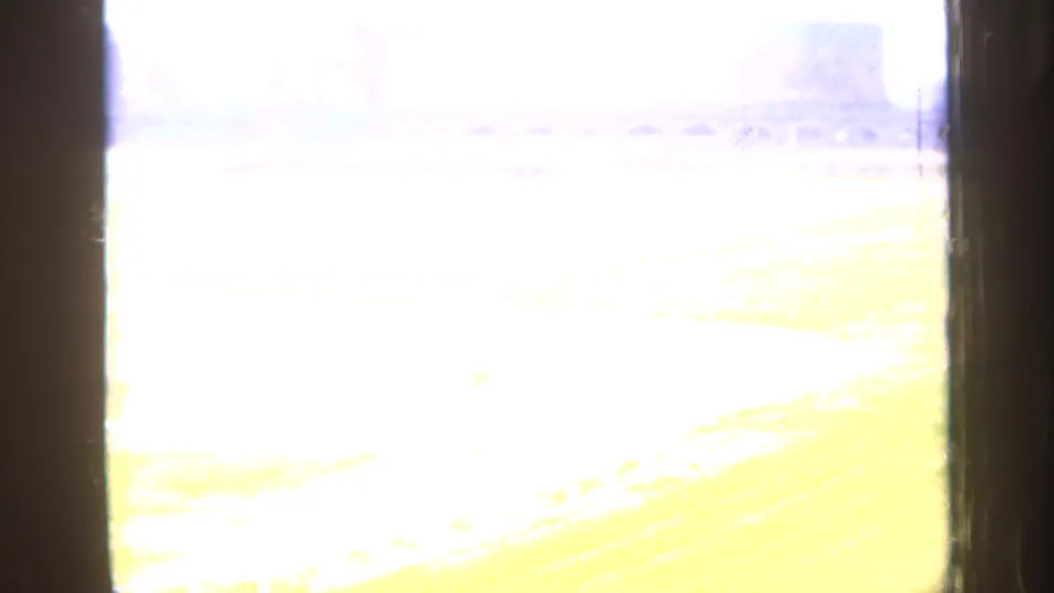 Overexposed 8mm transition frame from the 1949 England clip, with faint traces of an outdoor field and railings.