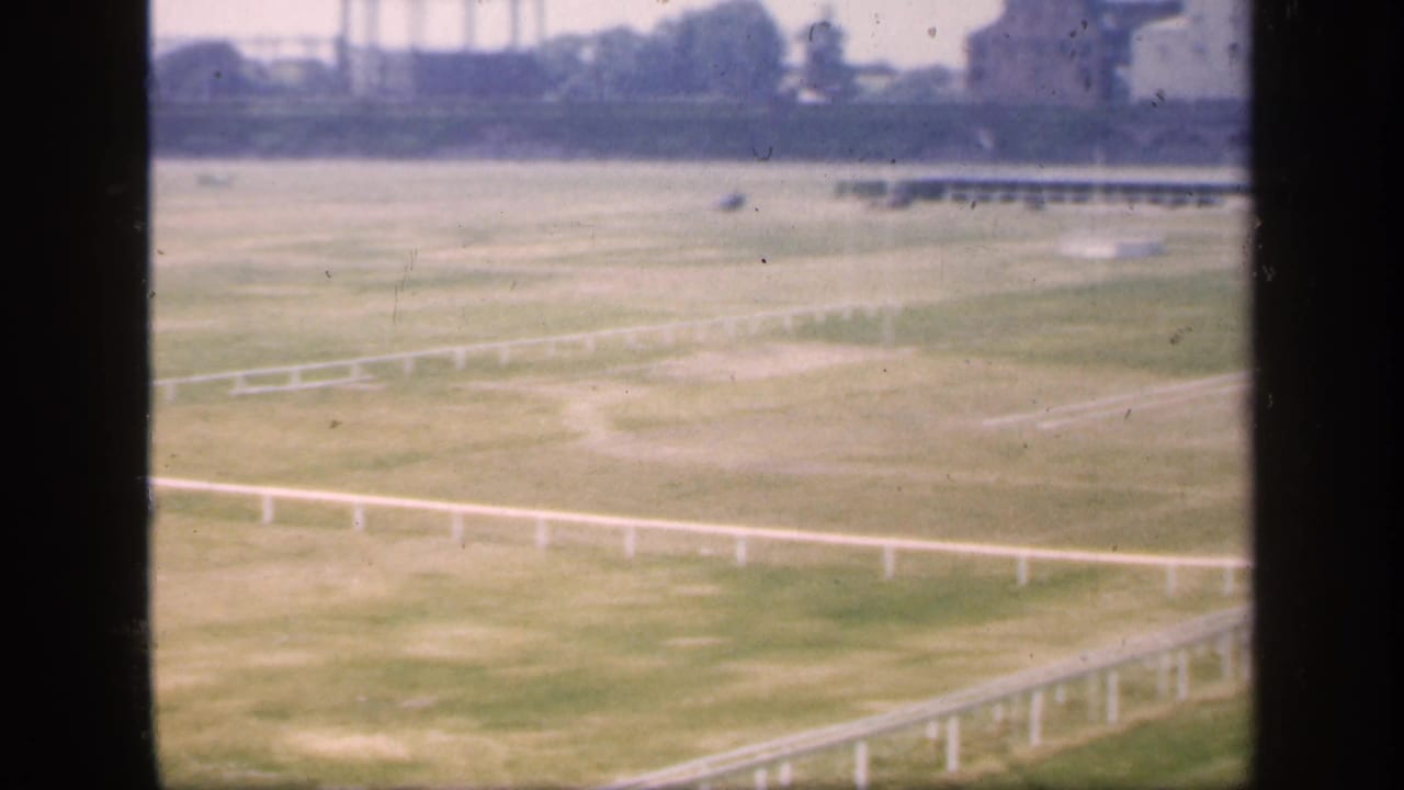 1949 England home-movie frame showing a broad grassy field and white railings viewed through a divided window.