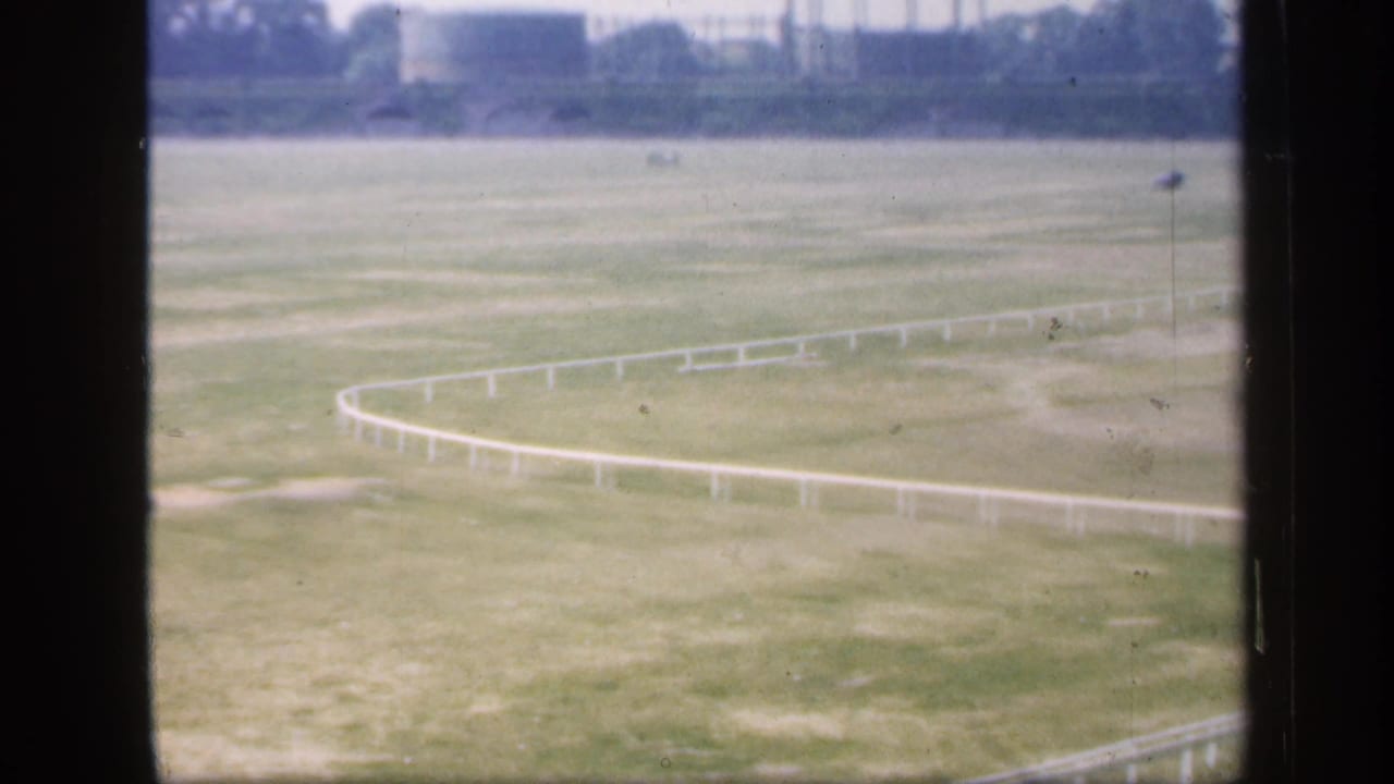 The camera pan continues across an English field with curving white railings, seen through the vertical and horizontal window bars.