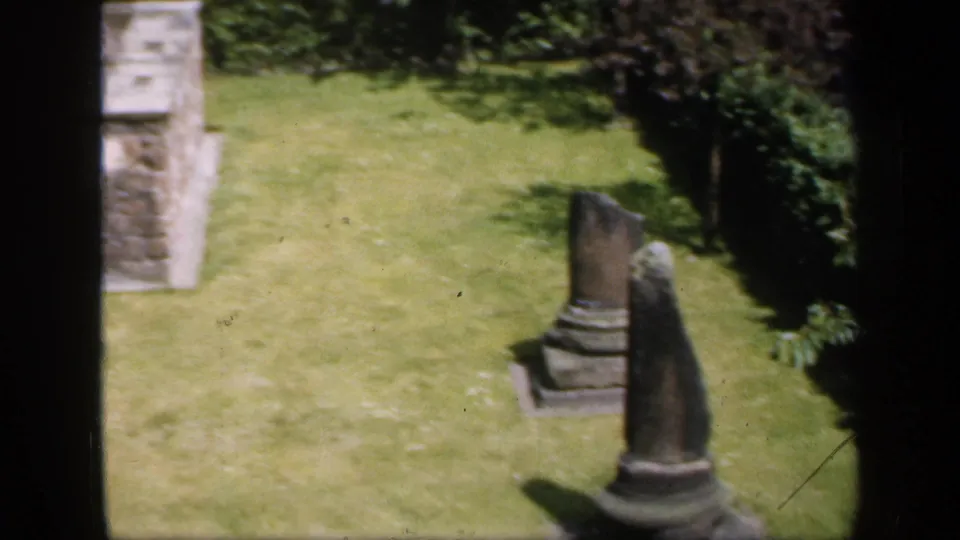 The final frame shows a manicured lawn with stone pillar-like remains and low masonry, still framed by the dark window bars.