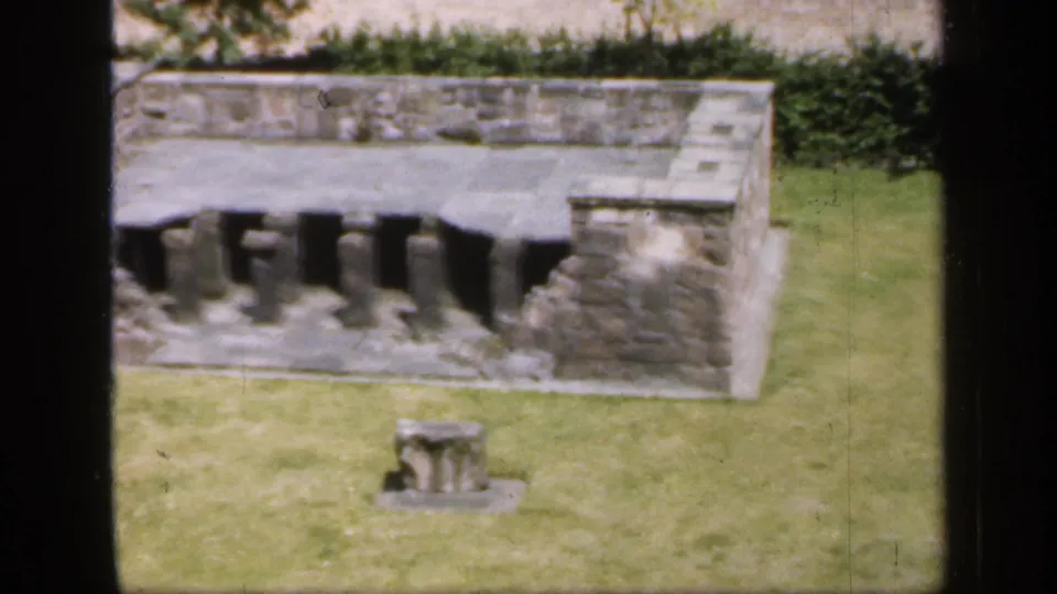 1949 England 8mm frame showing the ruin's arched masonry details, grass foreground, hedges, and a small stone remnant.