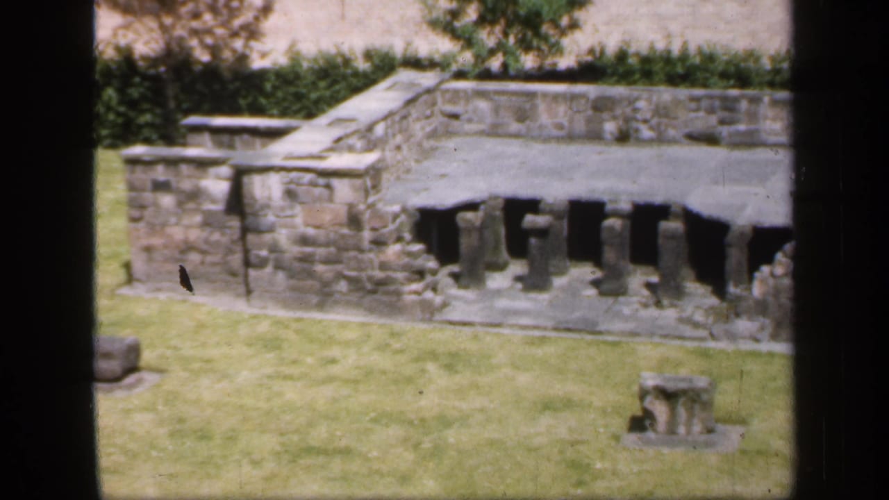 Low stone structure and lawn seen through dark film-frame borders.
