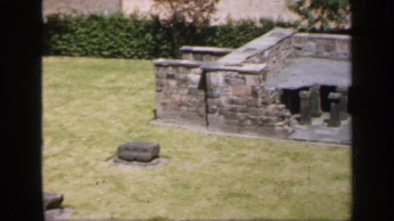 Stone wall section, lawn, hedge, and small stone marker.