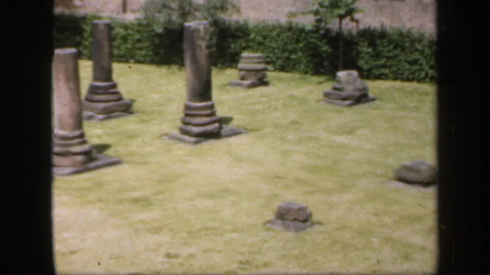 1949 England 8mm frame showing multiple grey stone columns and remnants arranged across a maintained garden lawn.