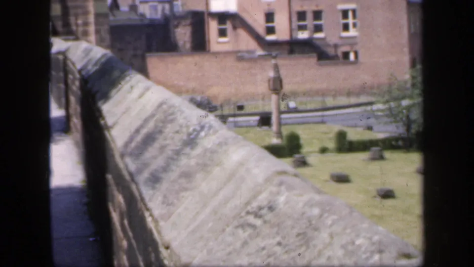 Stone walkway and parapet in England, 1949, looking toward a courtyard with markers, a small monument, and brick buildings.