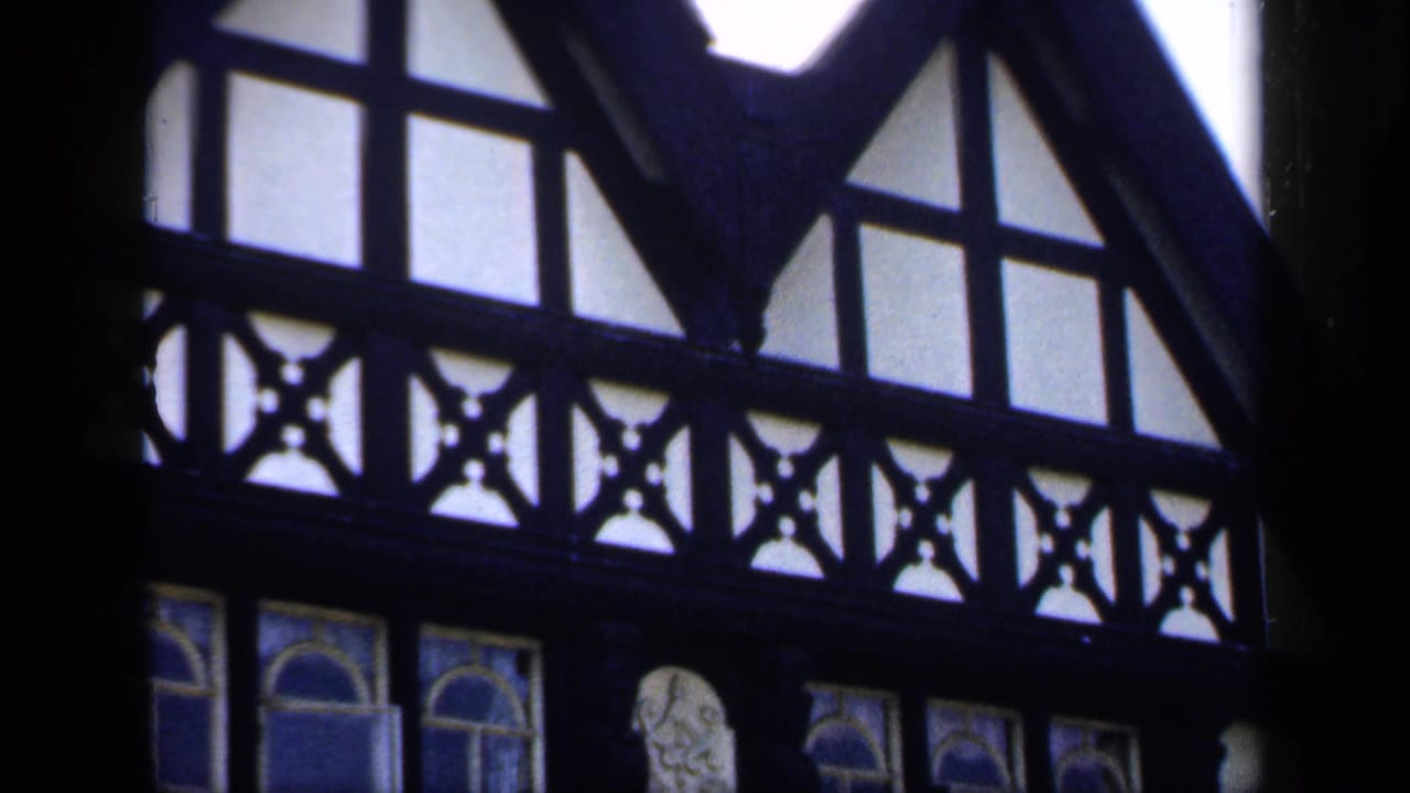 1949 England 8mm frame showing dark timber framing, high interior windows, and decorative arched glass inside a church-like space.