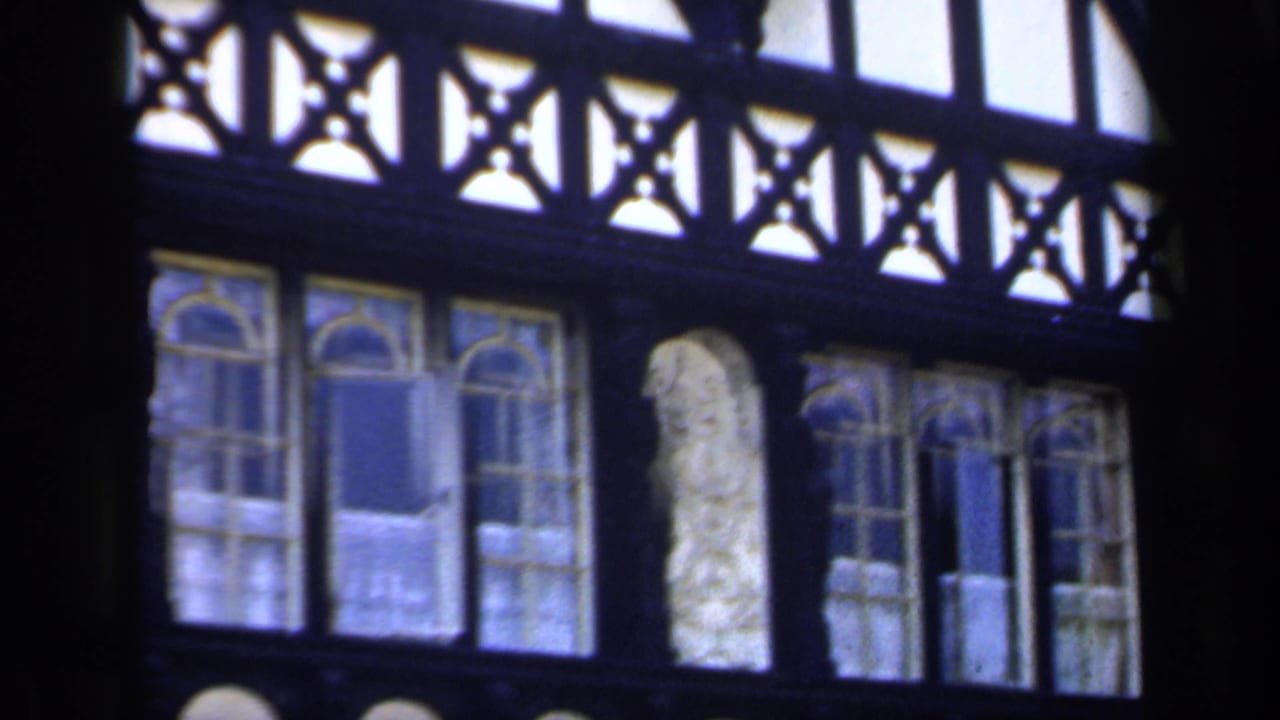 1949 England 8mm frame of an ornate church interior wall with timber tracery, stained glass, and repeated arched forms.