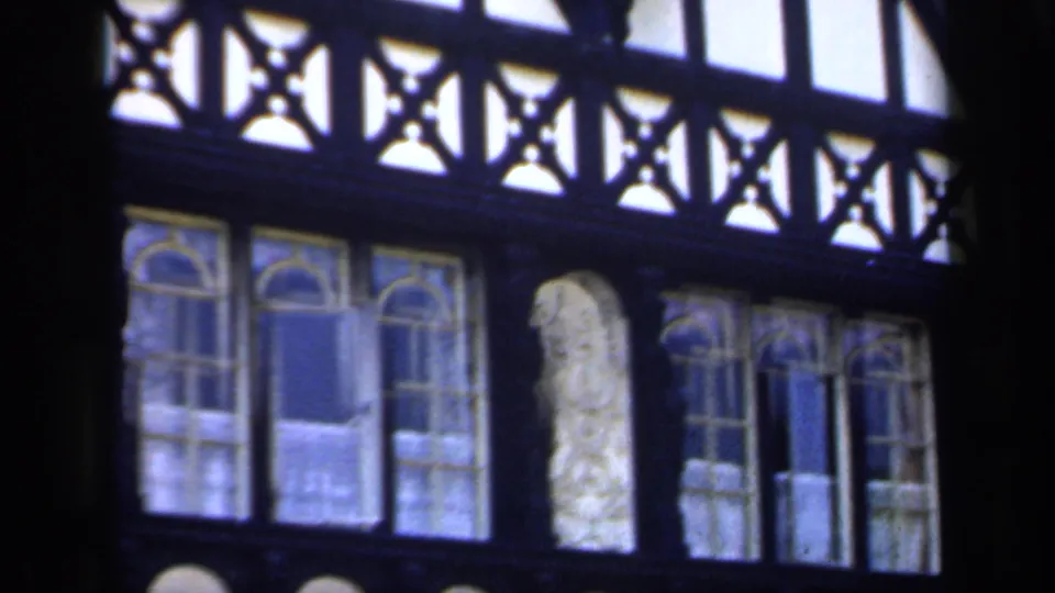 1949 England 8mm frame of an ornate church interior wall with timber tracery, stained glass, and repeated arched forms.
