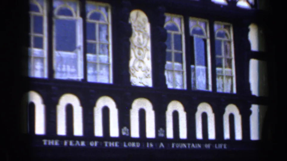 1949 England 8mm frame showing arched church windows, stained glass, and the visible inscription 'THE FEAR OF THE LORD IS A FOUNTAIN OF LIFE.'