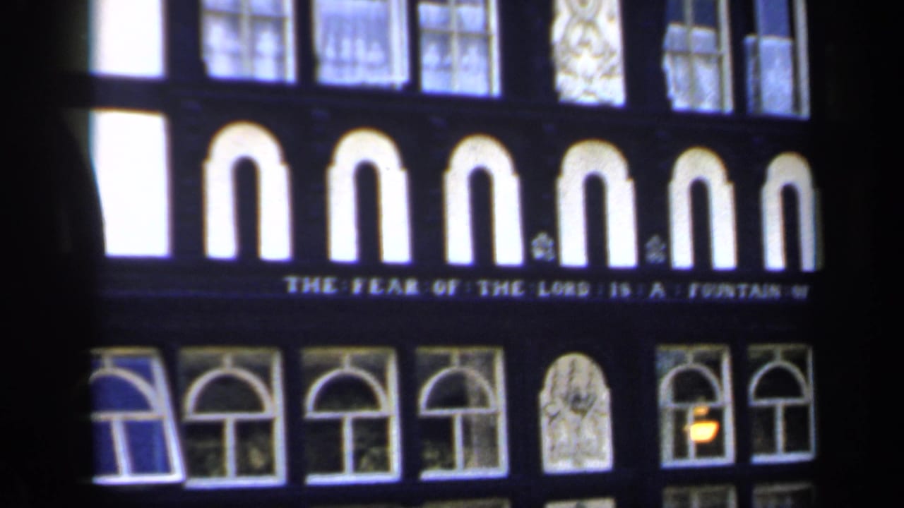 Close view of a black-and-white facade with arched windows and a biblical inscription.