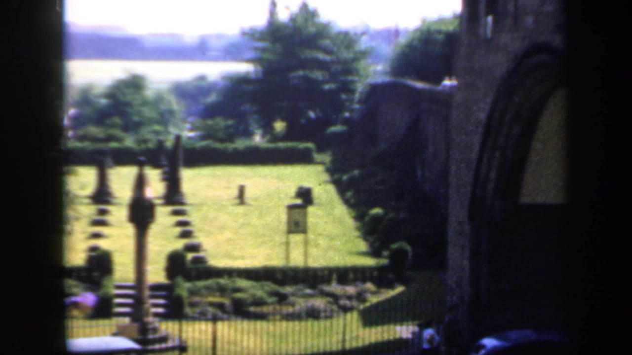 Garden lawn and stone building seen through a dark archway.