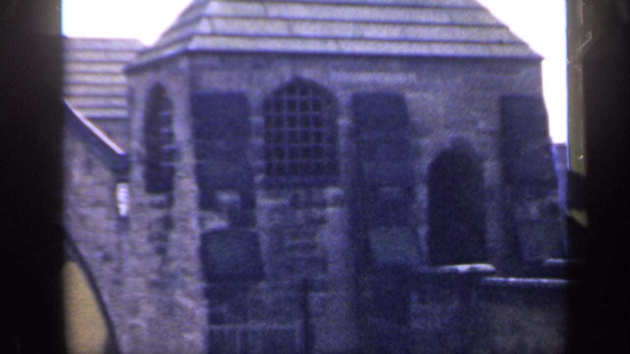1949 England 8mm frame showing a weathered stone building, arched windows, and dark foreground edges from the camera position.