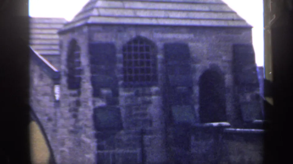 1949 England 8mm frame showing a weathered stone building, arched windows, and dark foreground edges from the camera position.