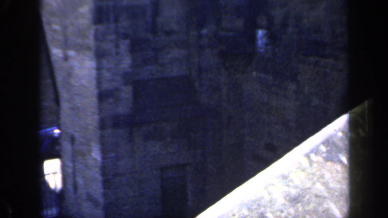 Dark 8mm frame showing a grey stone castle wall beside a bright angled foreground surface.