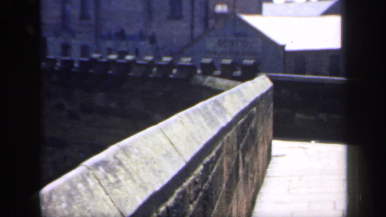 Narrow stone path with a high parapet wall and older buildings in the background.