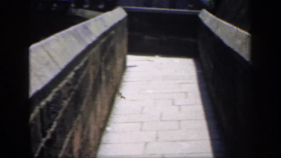 1949 England frame showing the stone walkway between parapet walls as the path angles into darker shade.