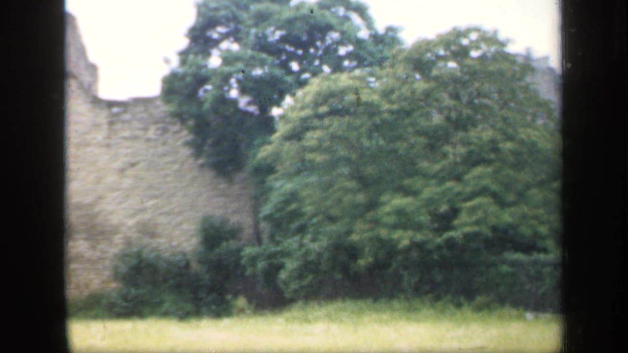 Stone ruin wall seen across a grassy lawn, partly framed by dark window edges.