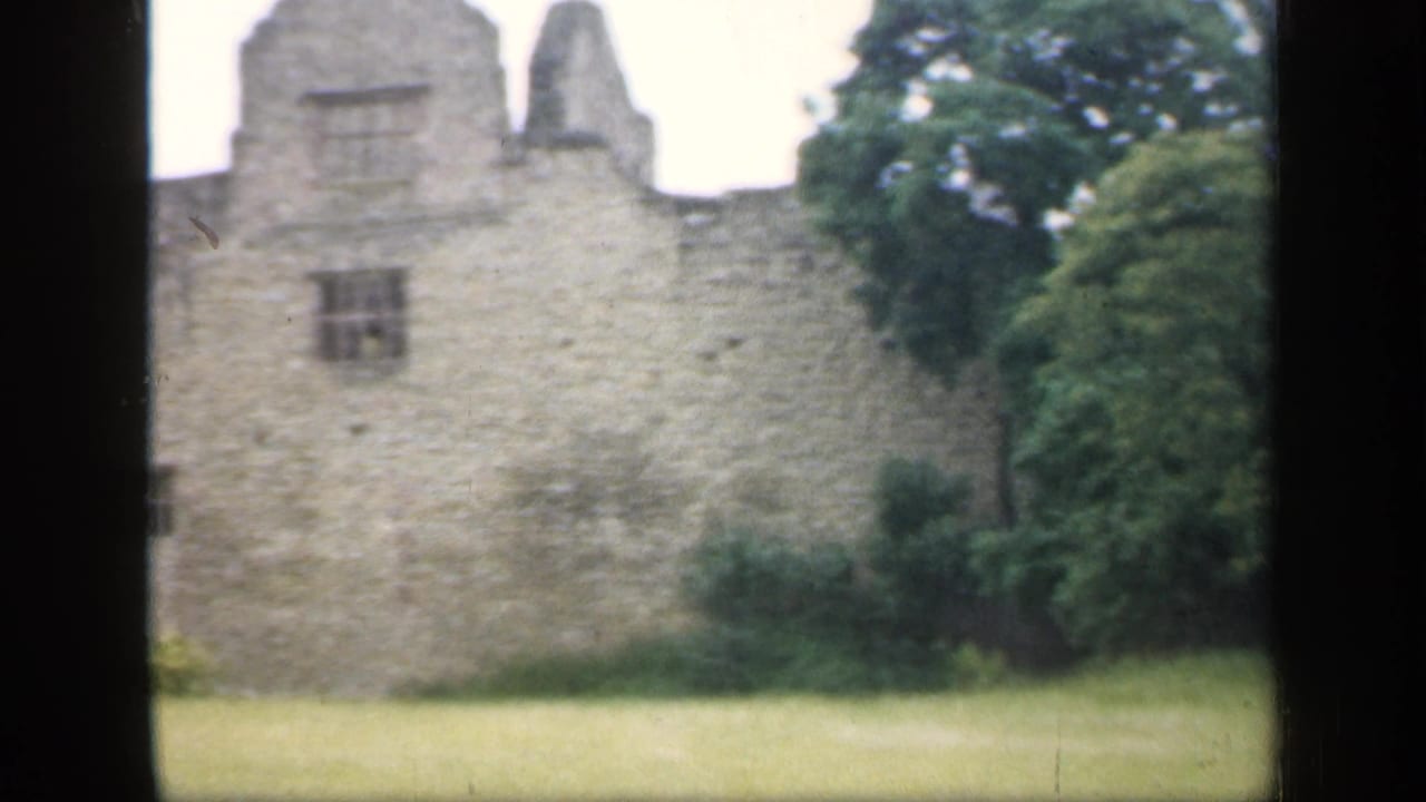 Central section of a stone ruin with small windows, lawn, shrubs, and trees.