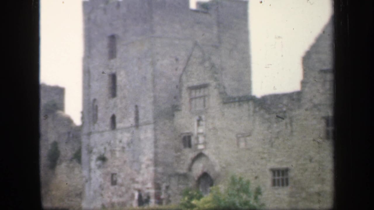 Handheld 8mm view in England, 1949, showing a stone castle tower, adjoining wall, arched entrance, and distant visitors.