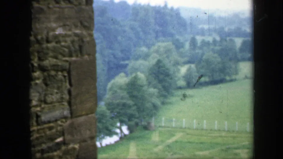 1949 England 8mm frame from near a stone structure overlooking green fields, trees, and wooded countryside.