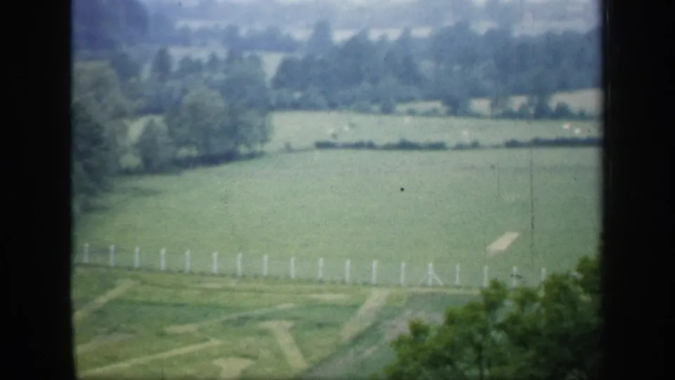 Rural English landscape in 1949 home-movie footage, showing fields, hedgerows, trees, and a pale fence through a dark frame.