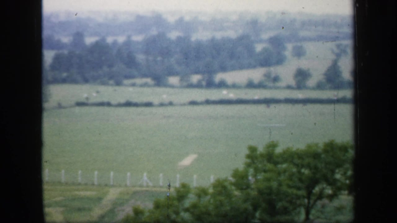 Green fields and hedgerows seen through a dark window frame.