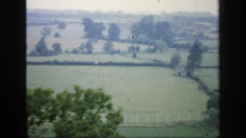 Final 8mm frame of the 1949 England countryside view, showing fields, hedgerows, trees, and dark window framing.