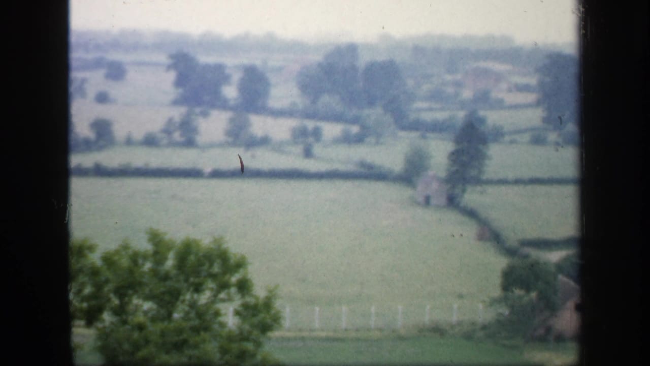 1949 England countryside view with hedgerow fields, distant trees, and dark foreground edges framing the landscape.