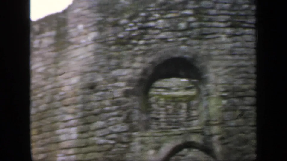 Close 1949 England home-movie view of a rough stone building or wall with a small arched opening.